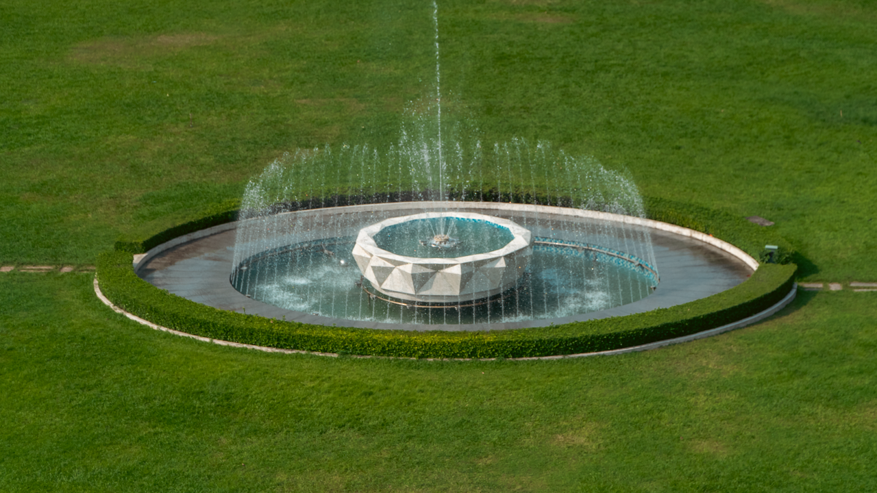 Aerial photo of an elegant geometric fountain surrounded by green grass.